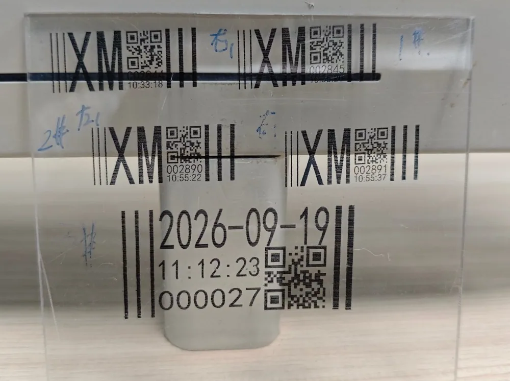 Several black codes printed across a transparent acrylic panel, with barcodes and a date code below them