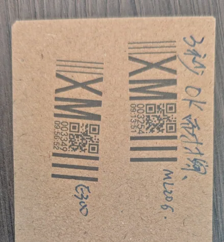 Two codes and their barcodes printed on a strip of uncoated kraft board, with handwritten notes beside them