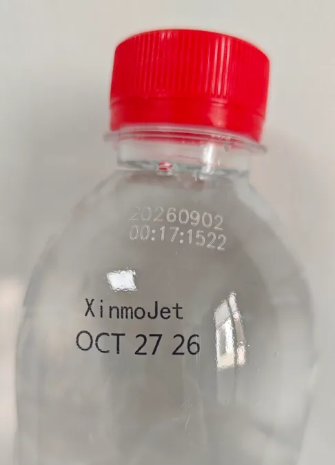 A clear PET water bottle with a red cap, carrying a faint grey date and time stamp above and a crisp black wordmark and date below