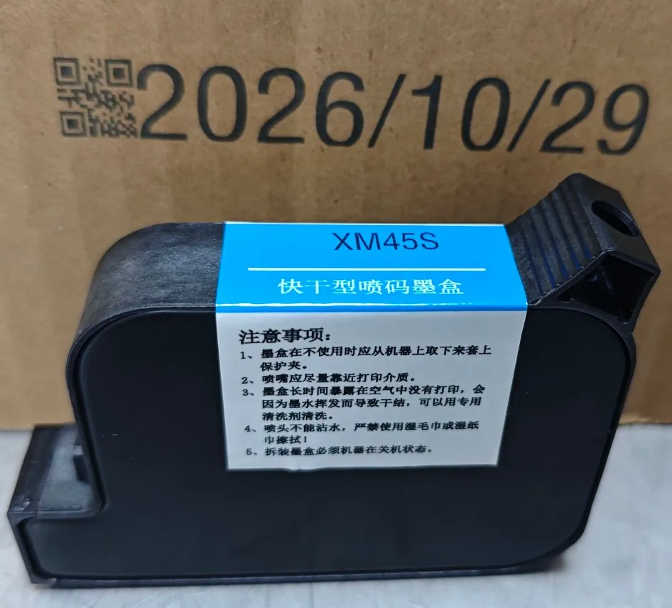 A solvent TIJ cartridge labelled XM45S standing on corrugated board, with a QR code and the date 2026/10/29 printed on the board behind it